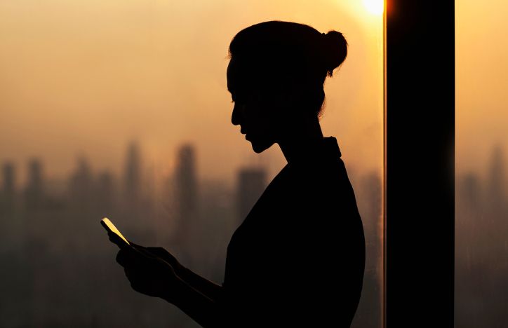 Silhouette Of Woman On Her Phone With City Skyline In Background