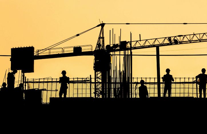 Silhouettes of construction workers and crane against a clear sky at dusk.jpg